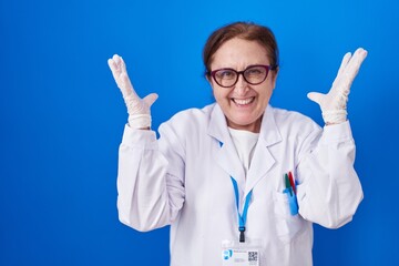 Poster - Senior woman with glasses wearing scientist uniform celebrating mad and crazy for success with arms raised and closed eyes screaming excited. winner concept