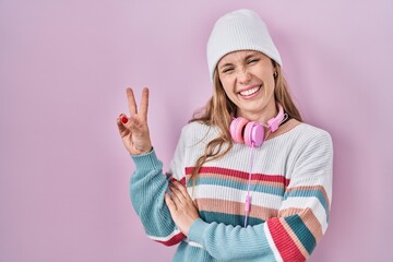 Canvas Print - Young blonde woman standing over pink background smiling with happy face winking at the camera doing victory sign. number two.