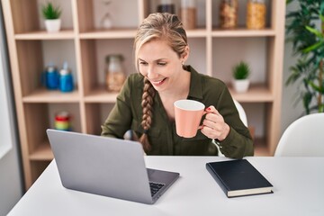 Poster - Young blonde woman using laptop drinking coffee at home