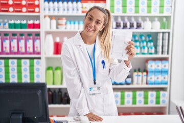 Young beautiful hispanic woman pharmacist smiling confident holding prescription paper at pharmacy