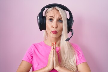 Wall Mural - Caucasian woman listening to music using headphones begging and praying with hands together with hope expression on face very emotional and worried. begging.