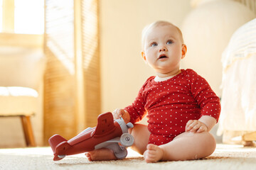 Wall Mural - Portrait of cute smiling baby, toddler sitting on bed with airplane toy at home