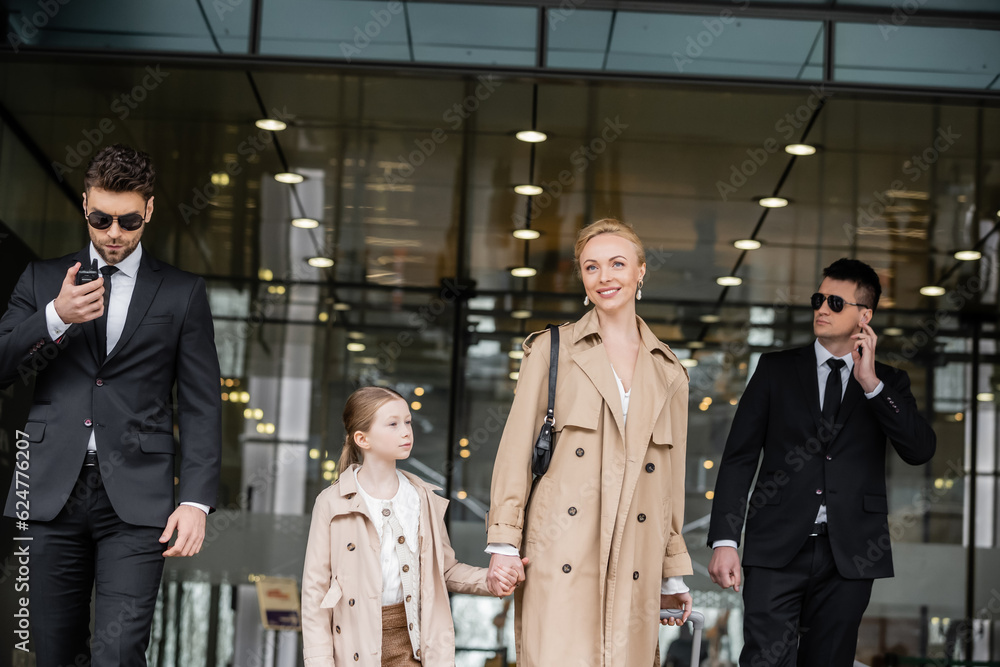 Photo Stock bodyguards walking next to cheerful woman and preteen kid ...