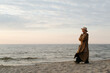 © Sergio - Thoughtful lonely stylish senior woman in brown coat and hat walking on beach in evening, copy space. Adult caucasian lady alone looking at sea