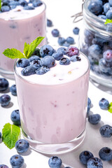 Wall Mural - Blueberry yogurt, smoothie or milkshake on portioned glasses with fresh blueberries decor on it, and a lot of fresh berries on white kitchen table background copy space