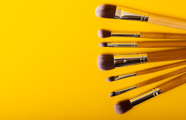 Wall Mural - Cosmetic makeup brush on a yellow background. Cosmetic product for make-up. Creative and beauty fashion concept. Fashion. Collection of cosmetic makeup brushes, top view, banner.Place for text. 