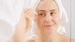 Smiling young woman wearing white towel plucking her eyebrows with cosmetic tweezers. Concept of beautiful female, makeup at home, skin care and domestic beauty industry.