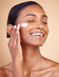 © Nadia L/peopleimages.com - Woman, happy skincare and cream for facial beauty, apply lotion and dermatology or cosmetics. Skin care product, face and young person or model sunscreen or moisturizer on a brown studio background