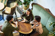 © pressmaster - Above angle of three young intercultural friends having chat while sitting by round wooden table in cafe or restaurant with vintage furniture