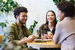 © pressmaster - Focus on two young friends looking at girl with smiles during discussion of plans or news while gathering by table in cozy cafe or restaurant