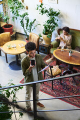 Poster - High angle of young male entrepreneur with mobile phone and financial documents talking on speakerphone against female colleague