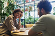 © pressmaster - Young cheerful African American woman laughing at jokes of her boyfriend while sitting by table in front of him and having coffee with dessert