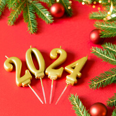 Wall Mural - Happy new year 2024 red background with gold number. Christmas card banner with round red balls toys, Christmas tree branches and golden decorative candles, bokeh lights. Mockup.