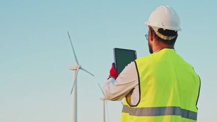 Wall Mural - Engineer in Wind Turbine park checks the status of the turbines using a tablet with chroma key green screen. Copy space mockup