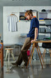 © LIGHTFIELD STUDIOS - Side view of young redhead craftsman in casual clothes standing near smartphone wooden working table in print studio at background, self-made success concept