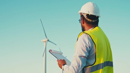 Wall Mural - Wind turbines generate green energy with zero carbon footprint. Engineer holding a clipboard and and takes notes on the operation of each turbine