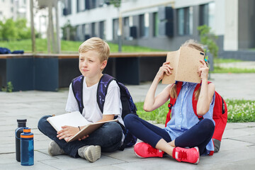 Wall Mural - Schoolchildren are bored reading books and studying homework in school yard. Mental health.