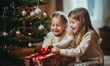 © ink drop - Two sisters open presents on Christmas day in front of the christmas tree