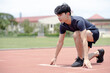 © Wanwajee - An asian man ready to run at start point with concentration emotion at sport field background.