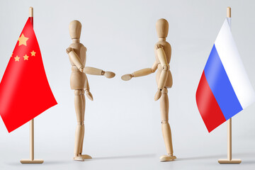 Two wooden men greet each other against the background of the flags of Russia and China