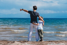 Father And Son Hugging On The Shore Of The Lake And Looking Away