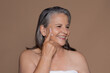 © Prostock-studio - Cheerful elderly caucasian lady with gray hair enjoys anti-aging treatment, applies cream