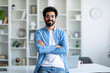 © Prostock-studio - Modern Entrepreneur. Handsome Young Indian Man Standing With Folded Arms Near Desk