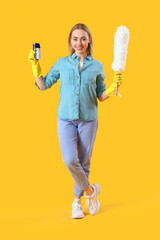 Wall Mural - Young woman with cleaning brush and pp-duster on yellow background