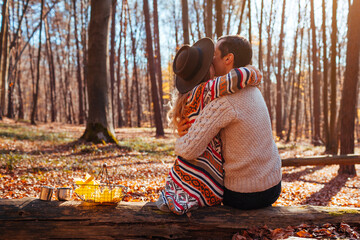 Wall Mural - Back view of couple hugging in autumn forest. Man and woman sitting on trunk enjoying fall landscape on date