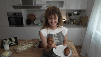 Wall Mural - happy young adult caucasian woman eat croissants in the kitchen