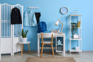 Wall Mural - Interior of workplace with desk, shelving unit, folding screen, clock and stylish school uniform hanging on blue wall