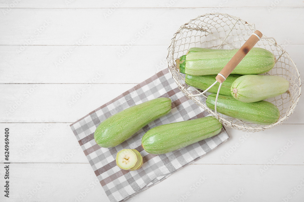 Basket with fresh green zucchini on white wooden background