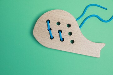 Poster - Wooden whale figure with holes and lace on green background, top view. Educational toy for motor skills development