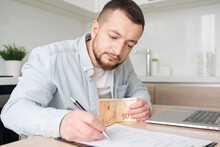 Business, Finances, Accounting And People Concept - Man With Money And Calculator Filling Papers At Home. Savings, Economy And Home 