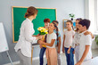 © Studio Romantic - Smiling children give the teacher a bouquet of flowers for the holiday. Teacher's Day celebration in the classroom on the background of the blackboard. A woman holds a bouquet of tulips in her hands.