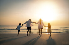 Family, Travel, Beach, Relax And Lifestyle, Holiday Concepts. Happy Family Are Having Fun At Beach In Sunset. Parents Are Holding Hands Their Children And Walking On The Beach At Sunset In Holiday.