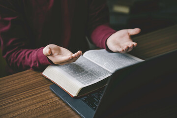 Wall Mural - Christian hands folded for prayer with a holy bible and laptop on a wooden table in church for worship online to god in the morning. person pray with faith, Spirituality, and religion concept