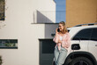 © Halfpoint - Young woman calling and charging her electric car in home, sustainable and economic transportation concept.