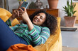 © ReeldealHD images - Young adult woman messaging friend lying on sofa