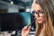 © peterzayda - Focused office worker in glasses with a pen in her hand touching her face.