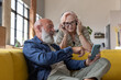 © ReeldealHD images - Trendy senior couple at home using a smartphone with headphones to listen to music