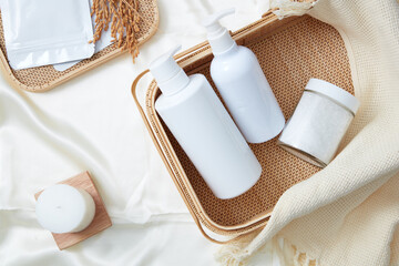 Advertising photo for cosmetic and product with bathroom concept. Two pump white bottle unbranded and jar of salt bath on bamboo basket decorated with scented candles on white fabric background