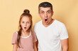 © sementsova321 - Shocked scared father and daughter wearing casual t-shirts standing isolated over beige background looking at camera with opend mouths and big eyes shock content.