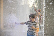 Boys jumping in water fountains. Children playing with a city fountain on hot summer day. Happy friends having fun in fountain. Summer weather. Friendship, lifestyle and vacation