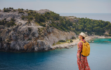 Wall Mural - Asian woman in hat look on views of azure Bay in Mediterranean sea. Travel and vacation concept. Anthony Quinn bay with crystal clear water in Rhodes island, Greece. The most beautiful beach.