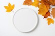 Empty white round coaster and yellow maple leaves on a white background.
