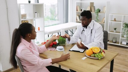 Wall Mural - Handsome african american man in white coat giving pills bottle to charming woman in consulting room of hospital. Male nutrition professional improving overall health with dietary supplements.