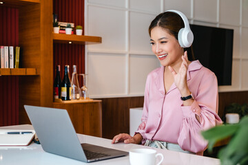 Canvas Print - Smiling asian woman freelancer wearing headset communicating with client via video computer call. .Millennial pleasant professional female tutor giving online language class.