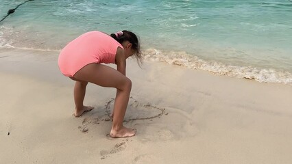 child playing in sea sand beach, little girl on tropical exotic sea coastline. the girl draws a hear