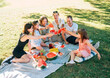 © Soloviova Liudmyla - Big caucasian family on picnic blanket on the in city park green grass. They rose-up red juicy watermelon pieces and clinking them like glasses. Family values and outdoor activities concept.